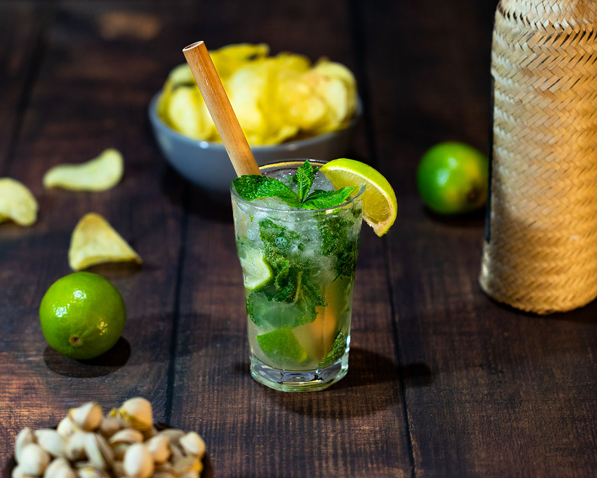 Photo d’une table d’apéritif estivale avec un cocktail Mojito, une bouteille de rhum, des chips croustillantes et des citrons frais, ambiance conviviale de soirée entre amis.