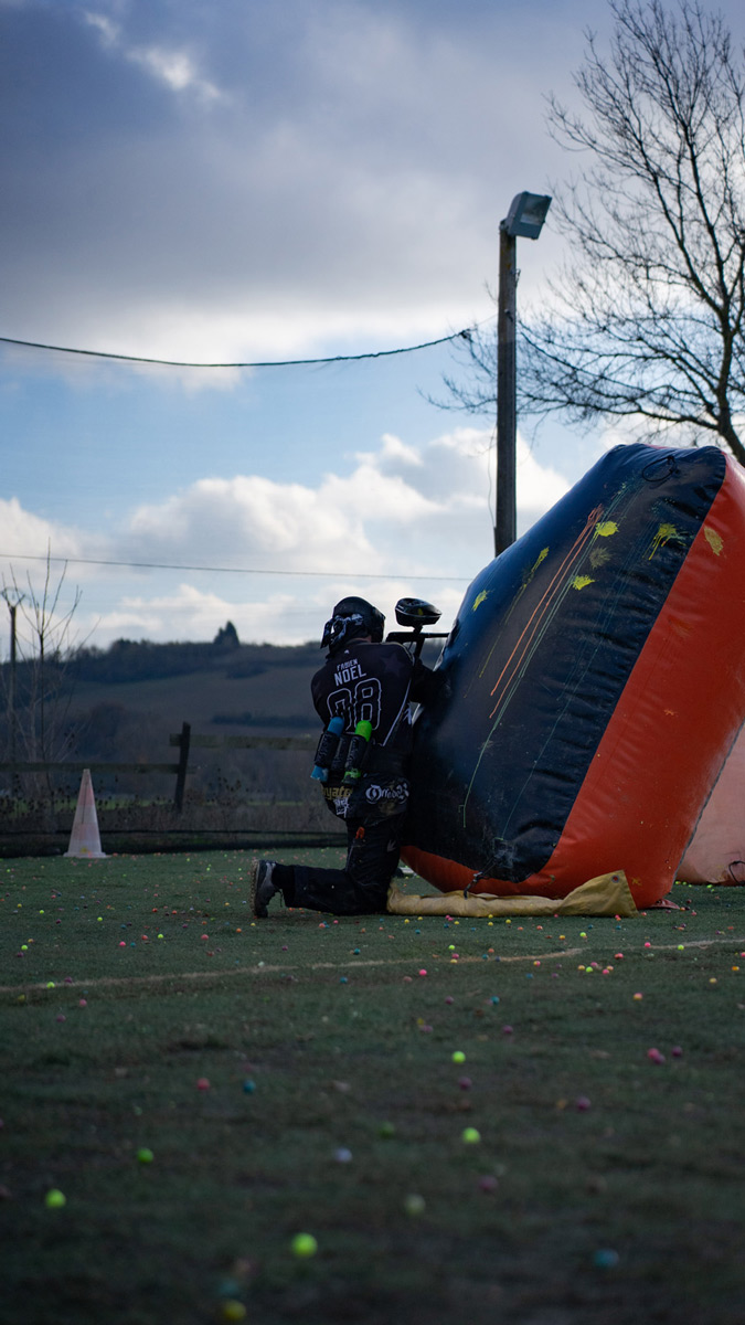Image d’un joueur de paintball à genoux derrière un obstacle gonflable, en position de défense sur un terrain extérieur lors d’une partie.