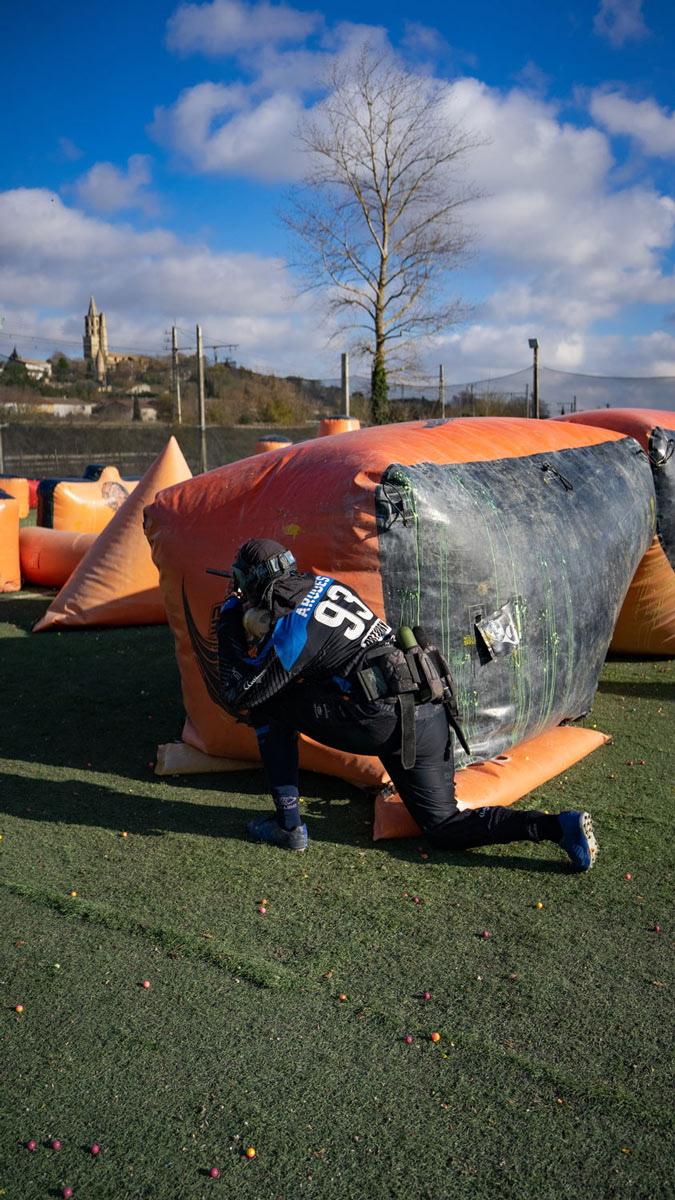 Joueur de paintball à genoux derrière un obstacle en attendant son adversaire